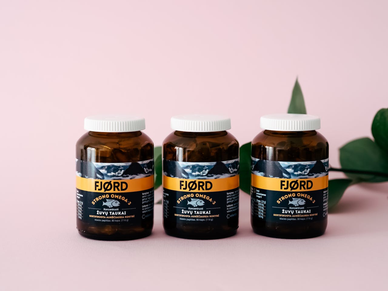 about-img Three FJORD Omega-3 supplement bottles on a pink backdrop with greenery accents.